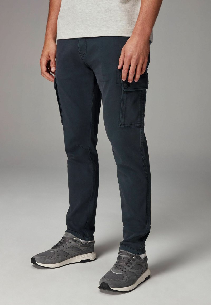 Dunkelblaue Cargo-Shorts aus einer Baumwollmischung mit zwei Seitentaschen. Sie verfügen über ein schlankes Design und eine glatte Textur, kombiniert mit grauen Sneakers.