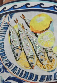 Vzorkovaná látka so zobrazenými rybami s flitrami, žlté citróny a modré akcenty na svetlom pozadí s detailnými prvkami dizajnu.