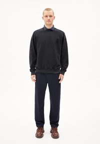 Dark grey sweatshirt with a round neck and long sleeves, paired with navy trousers and brown lace-up shoes. Features a subtle logo on the chest.