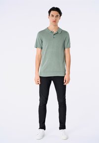Grön kortärmad polo med en tvåknapps placket, ribbad fåll och subtil textur, kombinerad med svarta slim fit-byxor och vita sneakers.