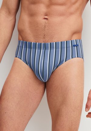 Man wearing blue and white vertical striped briefs, showing torso and upper legs against a plain background.