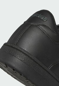 Černé kožené tenisky s texturovanou černou gumovou podrážkou. Obsahují prošívané detaily a embosované logo na patě.