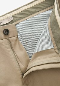 Beige katoenen broek met een rits en knoopsluiting. De binnenkant heeft een gestreepte en stippenvoering en extra zakken.