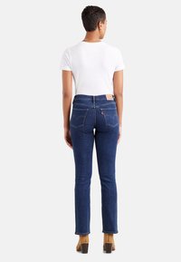 Dark blue denim jeans with a slim fit and straight leg, featuring back pockets with stitched detailing and a branded leather patch.