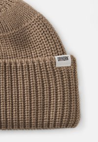 Gorro de malha castanho com textura canelada e dobra na aba. Apresenta um rótulo branco com o texto "DRYKORN".