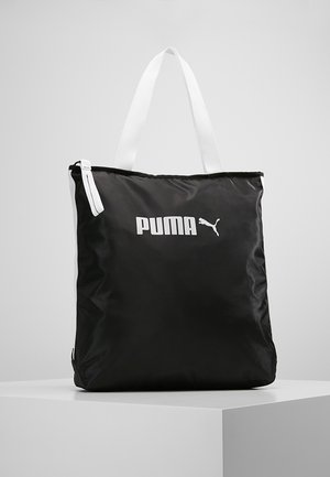 Schwarze Puma Tote-Tasche mit weißen Griffen und weißem Puma-Logo vorne, präsentiert auf einem weißen Podest vor einem schlichten Hintergrund.