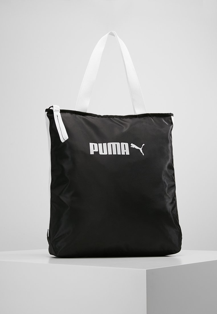 Sac cabas Puma noir avec poignées blanches et logo Puma blanc sur l'avant, présenté sur un socle blanc sur un fond uni.