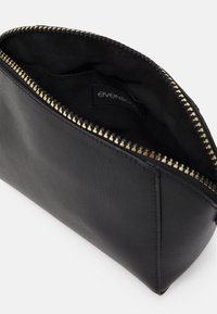 Necessaire per il trucco in pelle nera con superficie testurizzata e cerniera dorata, con rivestimento interno in tessuto nero e etichetta del brand all'interno.