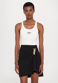 Hvit ribbet tanktop med en svart Moschino Jeans-logo, parret med et svart omslagsskjørt med en metallisk gullklipsdetalj.
