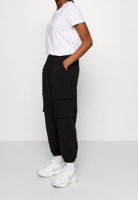 Pantalon cargo noir avec poches latérales, coupe ample, poignets élastiques, associé à un t-shirt blanc à manches courtes et des baskets blanches avec des accents lavande.