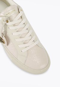 Kremowe sneakersy z teksturą imitującą skórę węża na palcach i bokach, z płaskimi sznurówkami oraz złotym akcentem logo na boku.