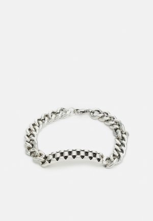 Pulseira de metal prateado com um design de corrente robusta, com elos lisos e uma seção central de tachas planas em forma de pirâmide. Fecho ajustável.