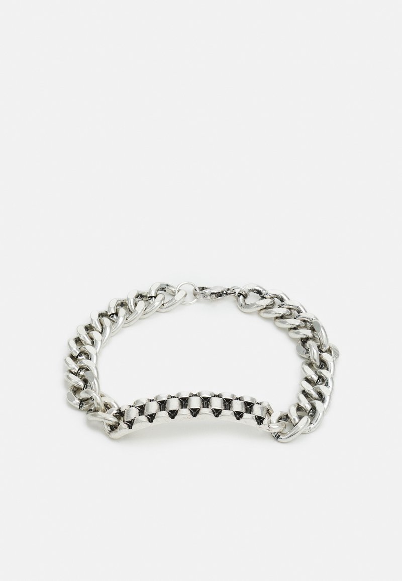 Pulseira de metal prateado com um design de corrente robusta, com elos lisos e uma seção central de tachas planas em forma de pirâmide. Fecho ajustável.