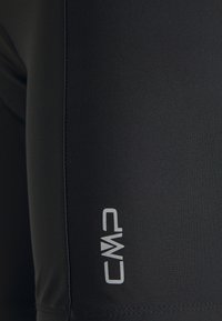 Gros plan sur un tissu noir avec une couture verticale et le logo blanc CMP imprimé près du bord inférieur.