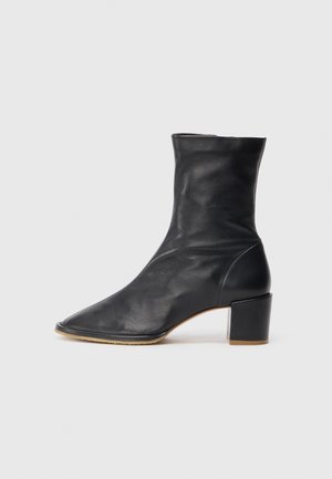 Juodas odinis kulkšninis botilienas su smailiu padu, prigludusia viršūne ir tvirtu kvadratiniu kulnu. Lygus paviršius su minimaliu siūlių išdėstymu.