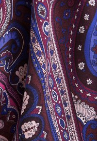 Tissu avec un motif paisley complexe en rouge profond, bleu, blanc et noir avec des détails floraux et abstraits.