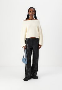 Pull en maille côtelé blanc cassé avec des manches larges, associé à un pantalon large en simili cuir noir et un petit sac à main bleu. Des chaussures noires viennent compléter le look.