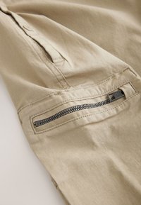 Beige fabric with a textured grid pattern. Features a zippered pocket on the side with metallic hardware, showcasing functional design elements.