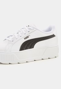 Sneaker bianca con accenti in pelle nera, dotata di una tomaia testurizzata, suola bianca spessa e design tradizionale con lacci. Marchio Puma visibile.