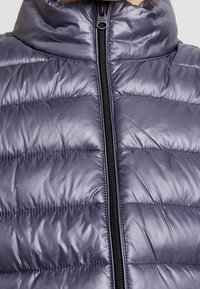 Vadderad nylonväst i mörkgrått med hög krage, utrustad med ett helfolierat blixtlås och ett horisontellt quiltat mönster. Slät, glänsande textur.