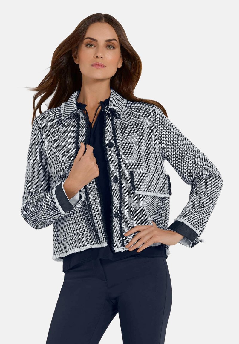 Marineblauw en witte houndstooth jasje met een cropped ontwerp, gescheurde randen, twee voorzakken en knoopsluitingen. Lange mouwen, kraag en contrasterende afwerking.