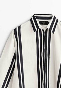 Chemise blanche à rayures verticales noires, dotée d'un col classique et d'une fermeture à boutons. Tissu lisse avec un design structuré.