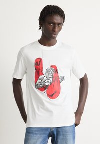 Mann trägt ein weißes T-Shirt mit einem Grafik von roten Boxhandschuhen und einem schwarz-weißen Boxer in einer Kampfpose.