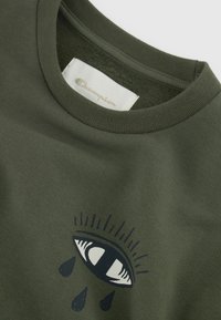 T-shirt verde oliva con scollo rotondo, caratterizzato da una grafica di un occhio e gocce sottostanti. Tessuto di cotone morbido, etichetta Champion visibile all'interno.