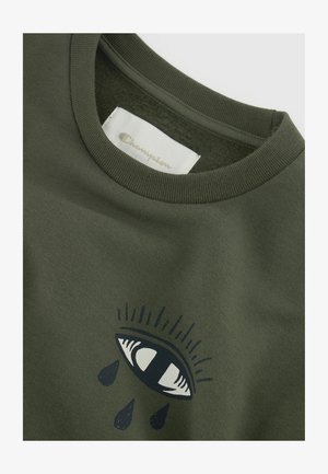 Camiseta verde oliva con cuello redondo, que presenta un gráfico de un ojo con gotas debajo. Textura de algodón suave, etiqueta de Champion visible en el interior.