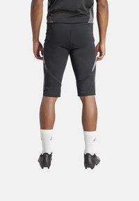 Zwarte sportieve shorts met mesh-zijpanelen, aansluitend ontwerp en subtiele stikdetails. Gedragen met witte sokken en zwarte voetbalschoenen.