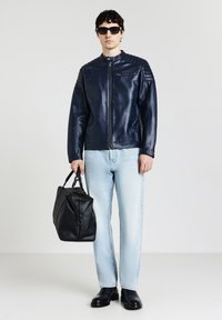 Veste en cuir marine avec une fermeture éclair et des détails côtelés aux épaules, associée à un jean bleu clair et des chaussures en cuir noir, portant un sac noir.