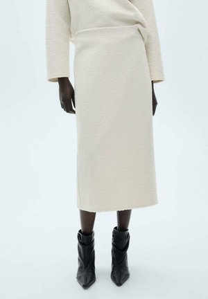 Cream, textured midi skirt with a straight cut and raw edges, paired with black ankle boots. Minimalist design, mid-rise waist.