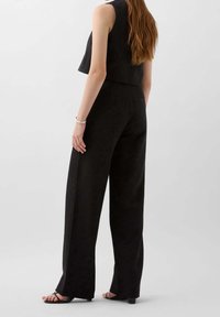 Svart kort ärmlös topp i kombination med högmidjade vida byxor, med en subtil textur och en smäcker design. Minimalistiska svarta sandaler.