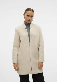 Abrigo de mezcla de lana color crema con un acabado texturizado, corte recto, sin cierre y con frente abierto. Presenta bolsillos laterales y un diseño sin cuello.