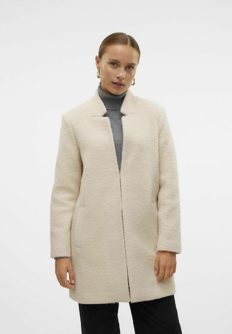 Abrigo de mezcla de lana color crema con un acabado texturizado, corte recto, sin cierre y con frente abierto. Presenta bolsillos laterales y un diseño sin cuello.