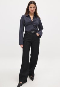 Tume sinine kraega särk, millel on nööbid, koos kõrge vöökohaga mustade avarate teksade ja terava musta kontsaga. Sile kangas.