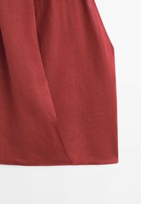 Tissu léger rouge drapé avec des coutures apparentes et une texture, sur un fond blanc uni.