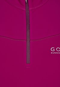 Fuksia zip-up juoksupaita, jossa on korkea kaulus, sujuva pinta ja heijastava logo etupuolella.