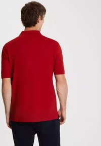Czerwona koszulka polo z krótkim rękawem, wykonana z gładkiego materiału, z klasycznym kołnierzykiem i prostym krojem. Gładki wzór, bez zdobień ani akcentów.