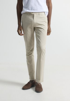 Chinos beige de algodón con corte slim, que presentan bolsillos frontales y una textura suave. Combinados con mocasines de ante marrón.