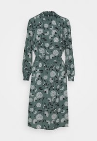 Robe verte à manches longues, col montant, taille élastique, et motif floral avec des fleurs blanches et des feuilles noires sur un fond uni.