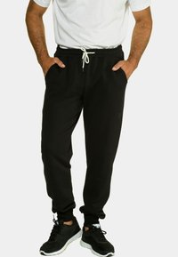 Zwarte sweatpants van een zachte stof met een elastische tailleband en trekkoord; voorzien van zijzakken en taps toelopende boorden. Gekocht met zwarte sneakers.