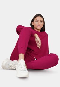 Bordeauxfarbenes Sweatshirt und passende Jogginghosen in einer entspannten Passform, aus weichem Stoff, kombiniert mit weißen Turnschuhen. Einfaches Design, ohne Muster.