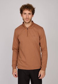 Polo shirt marron à manches longues avec un col zippé, fabriqué en tissu lisse. Présente des détails de logo subtils sur la poitrine.