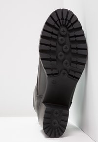 Semelle de botte en caoutchouc noir, présentant un motif de semelle profond avec des points de traction circulaires et en forme d'étoile. Taille indiquée comme 37. Texture lisse.