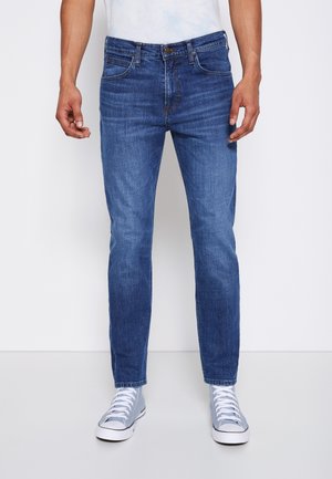 Blue denim jeans with a straight-leg cut, featuring front pockets, a zip fly, and subtle whiskering. Paired with gray canvas sneakers.