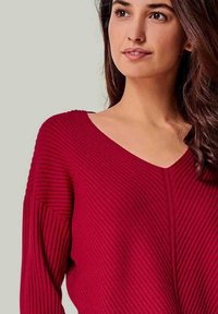 Roter gerippter Pullover mit tiefem V-Ausschnitt, der ein strukturiertes Gewebe, weite Ärmel und eine lockere Passform bietet.