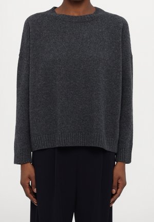 Pull en maille gris foncé à manches longues avec un col rond, porté avec un pantalon noir, visible des épaules aux hanches sur un fond uni.