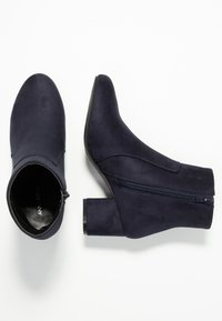 Bottines en daim bleu marine avec un bout pointu, une fermeture éclair latérale et un talon épais. Texture lisse avec des détails de coutures sur les côtés.