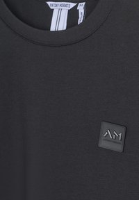Crna majica kratkih rukava od glatkog materijala, s teksturiranim logotipom kvadratnog oblika koji sadrži oznake "AM" i "ANTONY MORATO".